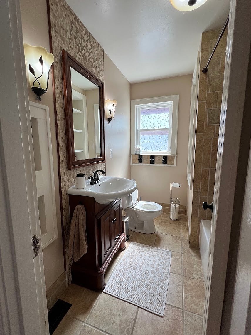 Bathroom has a shower and bathtub. Built-in shelves are located opposite the toilet and to the left of the sink. Perfect for holding towels, bathroom essentials, and makeup/accessories. Medicine cabinet behind mirror for additional, convenient storage.