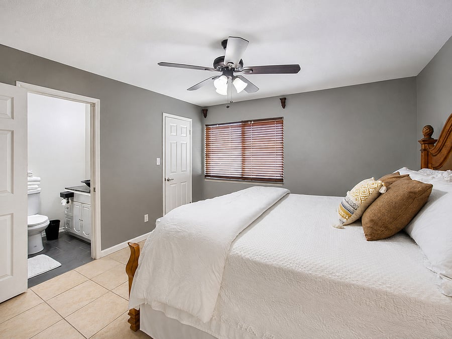 Relax in a spacious room featuring cool tile floors, a breezy ceiling fan, and crisp linens.