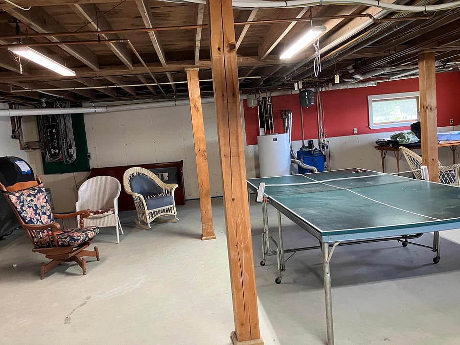 The partially finished basement has a Ping-Pong table and a cornhole game. The stairs to the basement are at the back of the living room and there is a gate at the top.