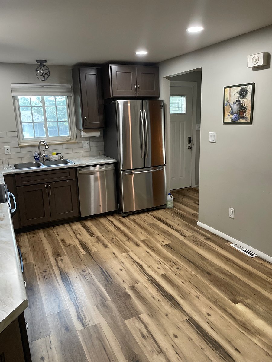 Kitchen with front door to the right of the fridge. Dishwasher, fridge and two compartment sink. Window above sink looks out to the front yard.