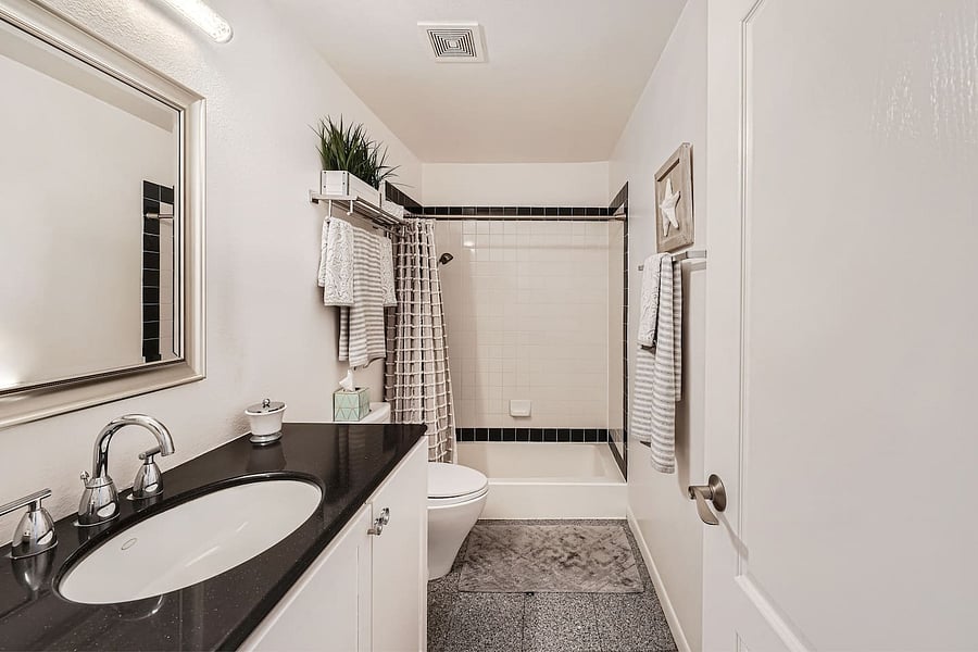 A clean, well-appointed bathroom featuring a spacious vanity with a black countertop, large mirror, and a tub/shower combination.