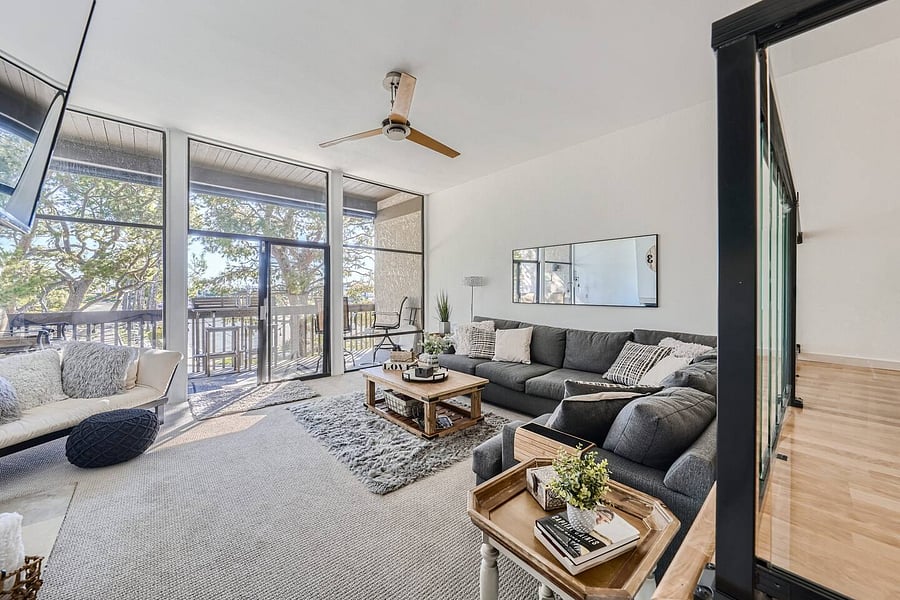 Floor-to-ceiling windows and glass doors fill the living spaces with natural light while offering views of the surrounding trees and balcony.