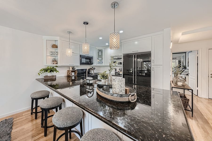 White cabinetry, dark stone countertops, hardwood-style flooring, and modern pendant lighting create a polished yet welcoming interior.