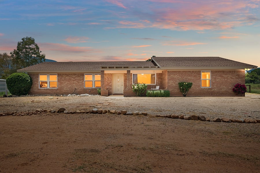 Welcoming single-story brick home photographed at sunset, with a covered front porch and warm exterior lighting.