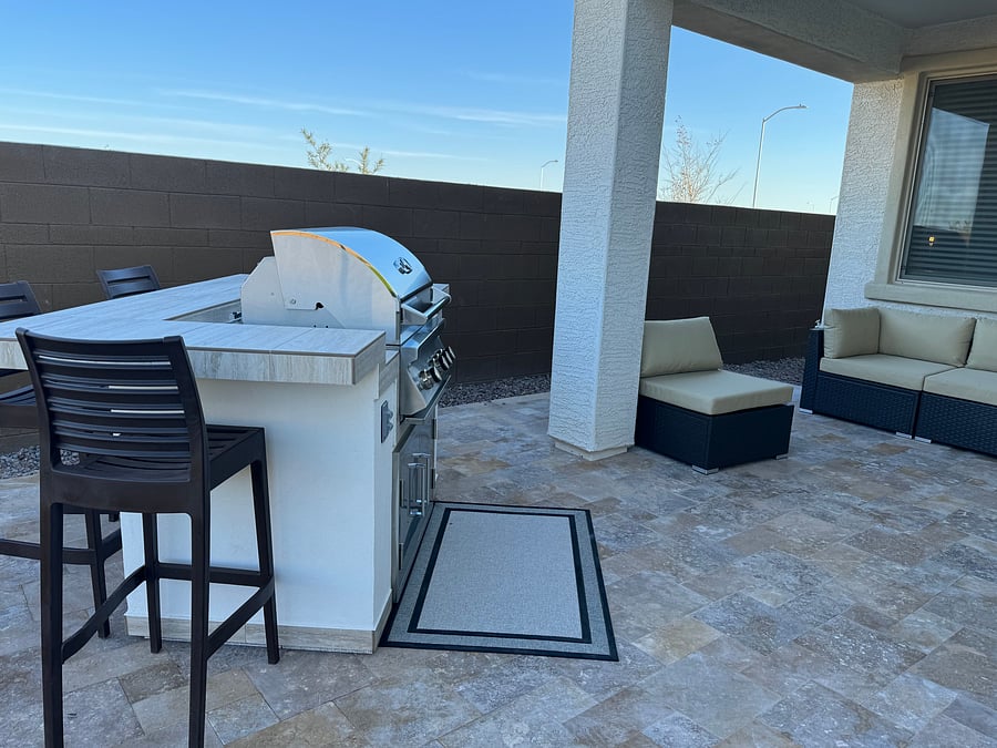 Built in barbeque with bar seating,  outdoor sofa seating, firepit, and travertine pavers.  Artificial turf is on the rest of the yard with shrubs at the perimeter.
