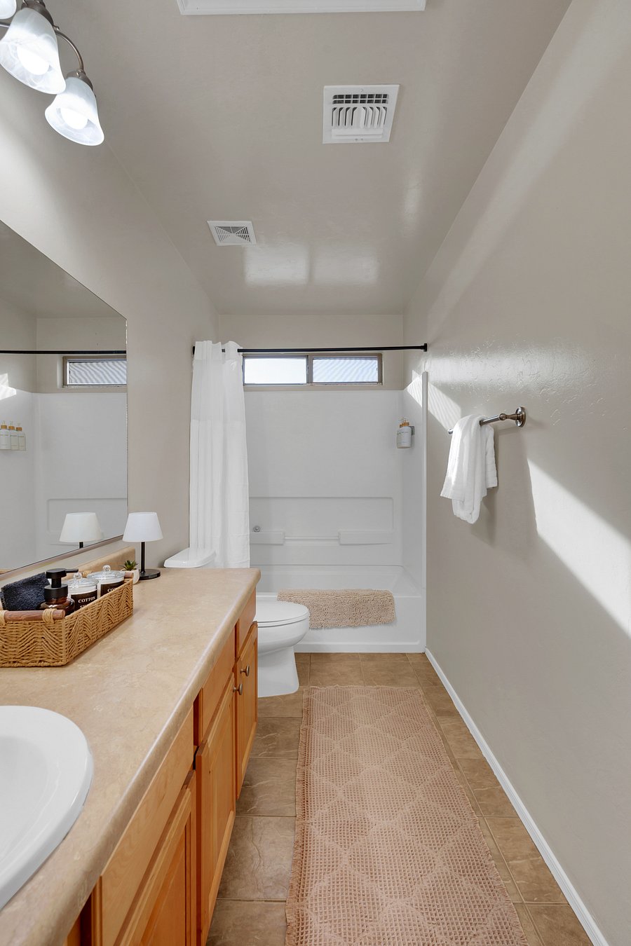 A bright, spacious bathroom with a full tub and shower, a long vanity, and plush white towels.