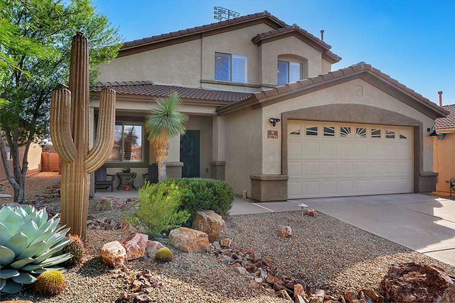 Welcome to your desert retreat: a stylish two-story home with warm porch lighting, lush desert landscaping, and an inviting curb appeal.