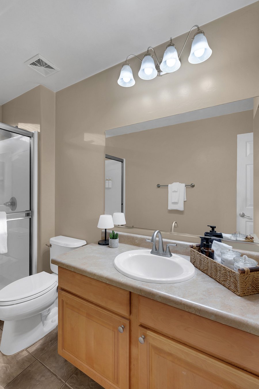 A clean, inviting vanity with a large mirror, soft lighting, and a woven basket of guest essentials.