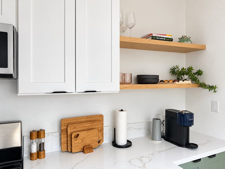 Thoughtfully equipped kitchen with a Nespresso coffee maker, quartz countertops, natural wood shelving, and modern sage-green cabinetry.