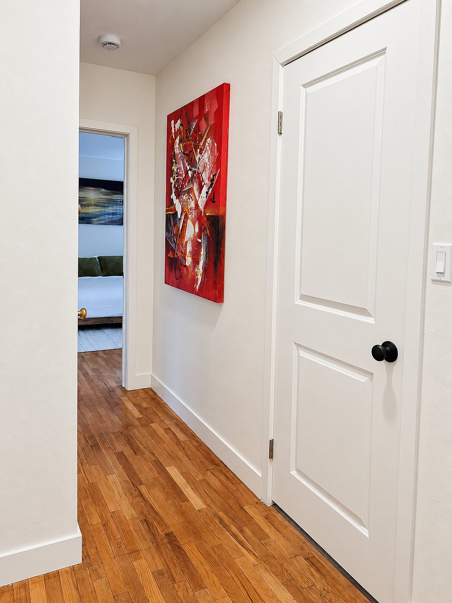 Bright hallway with refinished hardwood floors, fresh white walls, and colorful artwork connecting the living areas and bedrooms.