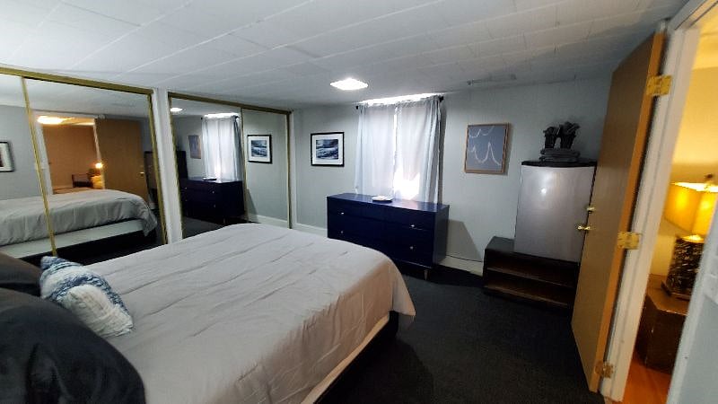 Bedroom has an egress window with black-out curtains, a dresser and a mini-fridge.