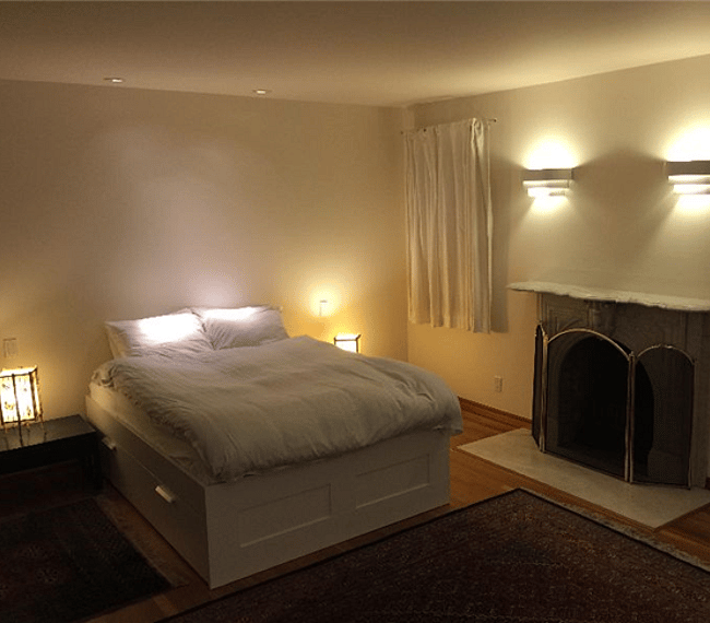 The Main Bedroom at night with lights lit at bedside and above fireplace