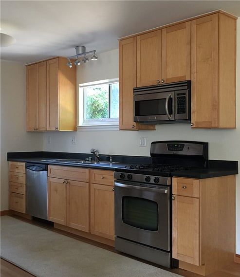 Kitchen and cabinets at the end of the studio space. 4 burner natural gas stove, dishwasher, two compartment sink, microwave-hood