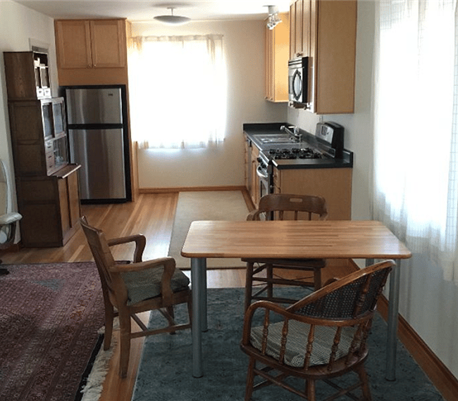 A view down the east side of the studio showing dining table, galley kitchen, tea cabinet and refrigerator