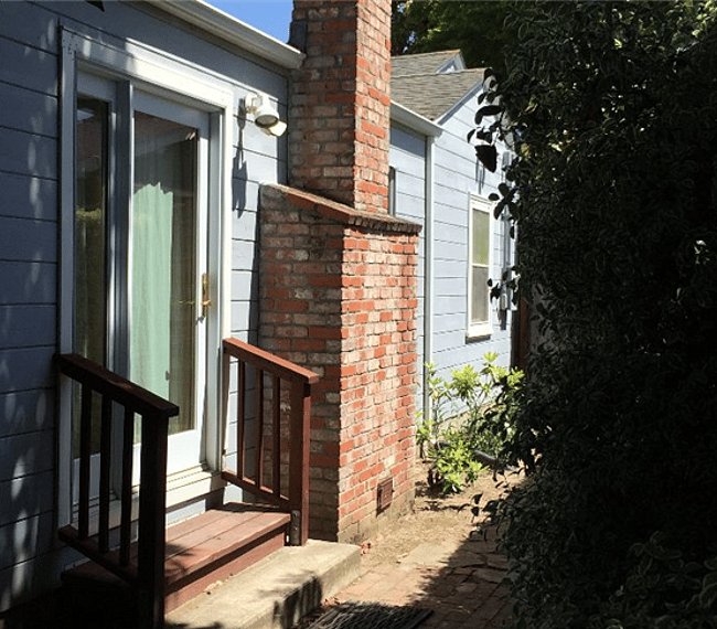 Two-step entrance to the studio from the outside with redwood railings. The decorative fireplace chimney is next to the steps. 