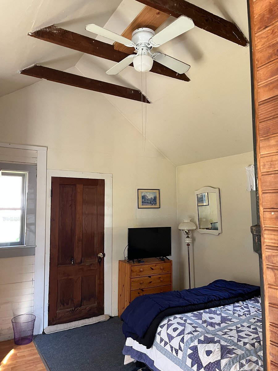 The bedroom opens up to the full one story-and-a-half of the cottage (and has both ceiling light and fan). In the bedroom, there is a second exterior door on the cottage. There are storm/screens throughout the cottage, and the bedroom door is double-insulated in winter.
