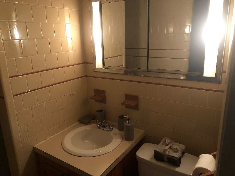 The bathroom is tiled from floor to ceiling with a vintage lighted vanity.