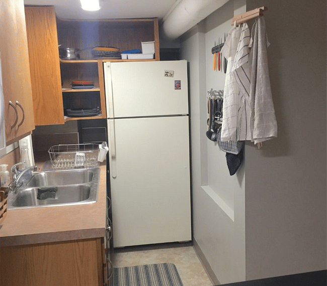 Looking down the galley kitchen to the refrigerator. Kitchen towels, utensils, are hanging on a magnetic wall rack.