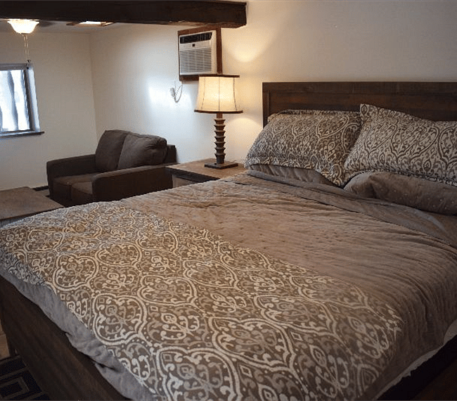 Cozy bedroom with king size bed, night stand, lamps and stuffed chair