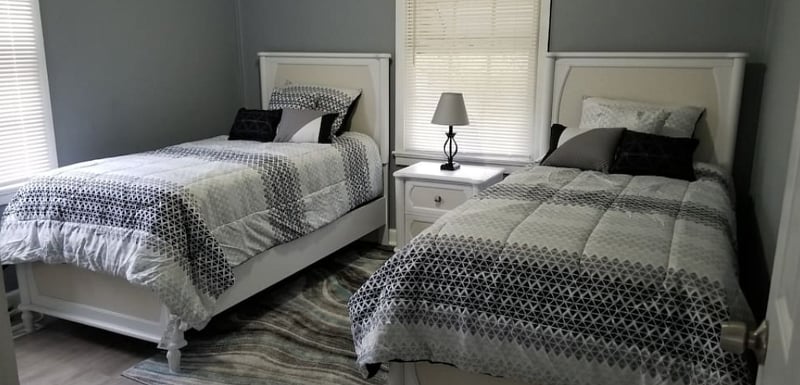The White Room - Features (2) soft but firm Twin Beds with plush pillows, a full dresser with mirror, night stand & lamp with colored smart bulb controlled by Google Assistant.