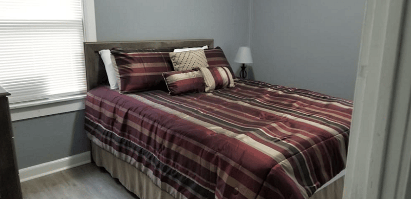 The Brown Room - Features (1) soft but firm Queen Bed with plush pillows, a dresser, night stand & lamp with colored smart bulb controlled by Google Assistant.
