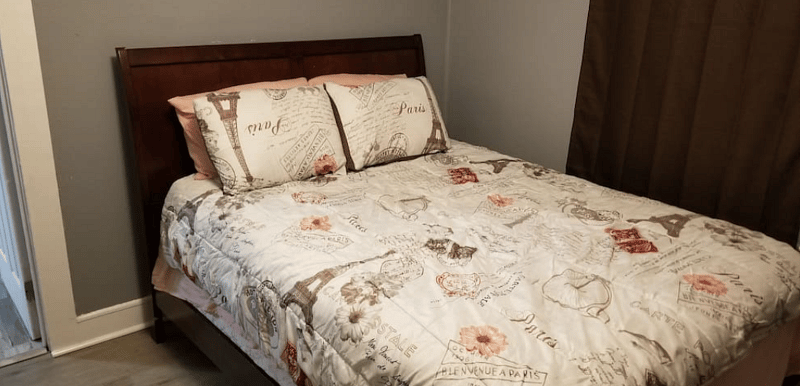 The Back Bedroom - Features (1) soft but firm Queen Bed with plush pillows, a dresser, night stand & lamp with colored smart bulb controlled by Google Assistant.