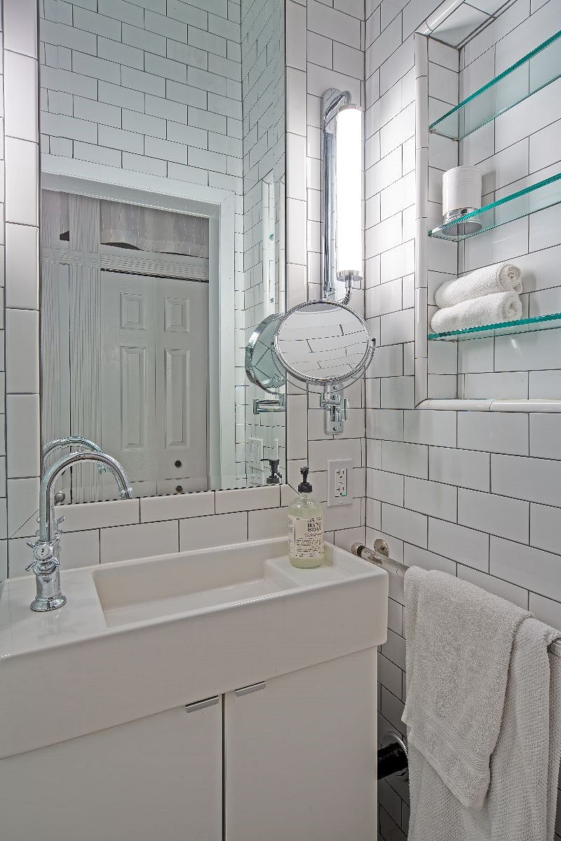Tile-lined bathroom with bright dimmable lights and open shelving.