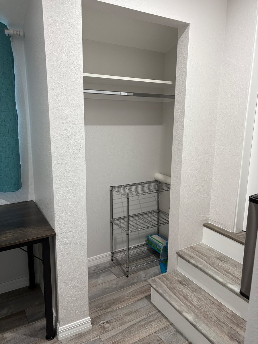 Closet with shelf above hanging rod for clothes; added shelf on the floor for shoes, or other items. Small vacuum, broom and mom cleaning supplies in the corner.
