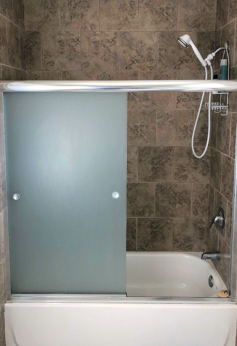 Marble-tiled shower features an adjustable shower head and frosted sliding doors.