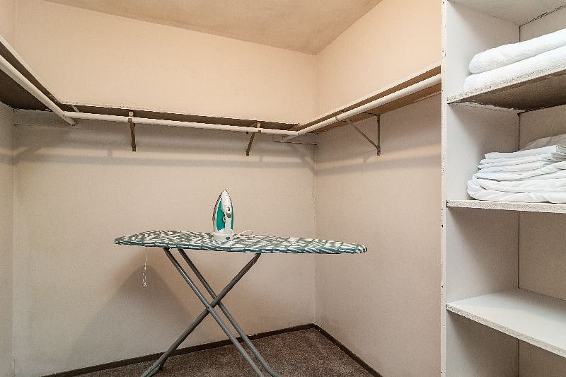 Huge walk in closet with iron, ironing board and clothes hamper.