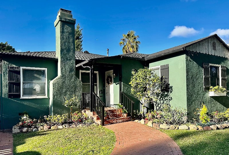 Beautiful landscaping includes citrus trees, leafy foliage and aged-brick pathways. Painted black wood trim, porch railings and cottage shutters add a contrasting accent.