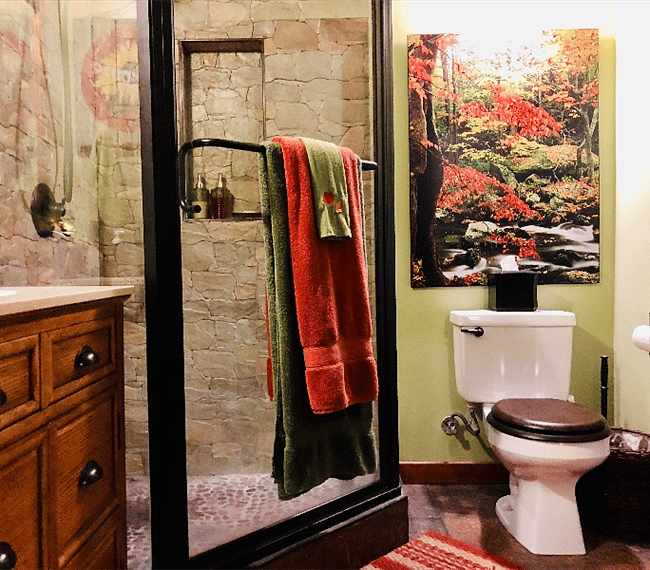 An oversized glass-encased shower, featuring oil-rubbed bronze fixtures, stone tiling with natural pebble floor, and an overhead skylight brings in the outdoors.