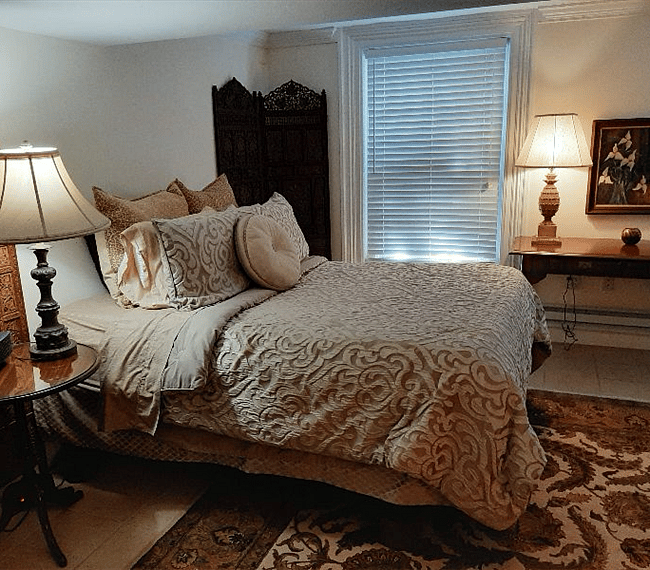 Cozy queen sized bed with a nightstand and a lamp