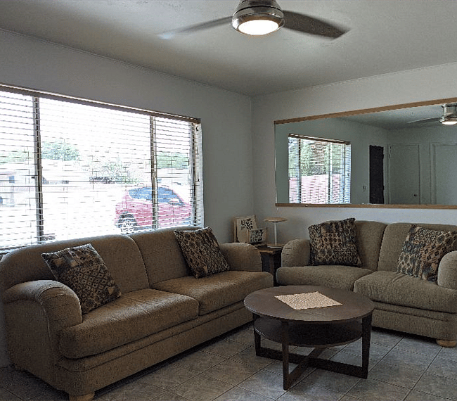 Living room with open windows, comfortable couch, ceiling fan/light.