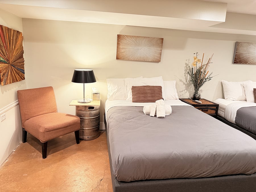 Wake up refreshed in this warmly lit bedroom featuring two queen beds, stylish nightstands, and curated wall art, with a classic arcade game waiting just steps away.