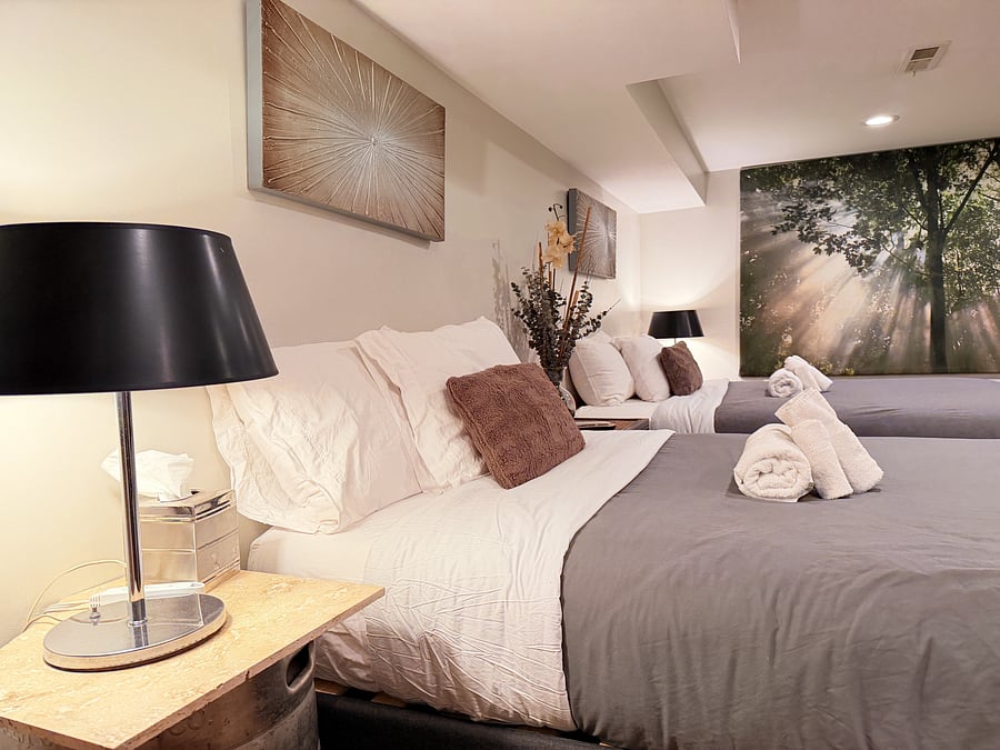 Wake up refreshed in this warmly lit bedroom featuring two queen beds, stylish nightstands, and curated wall art, with a classic arcade game waiting just steps away.