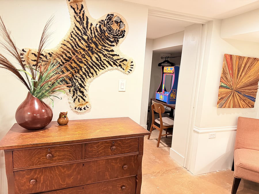 A unique hallway connects your bedroom, private bathroom, and game space, featuring a vintage dresser, bold tiger wall art, and vibrant greenery, every corner is filled with character.