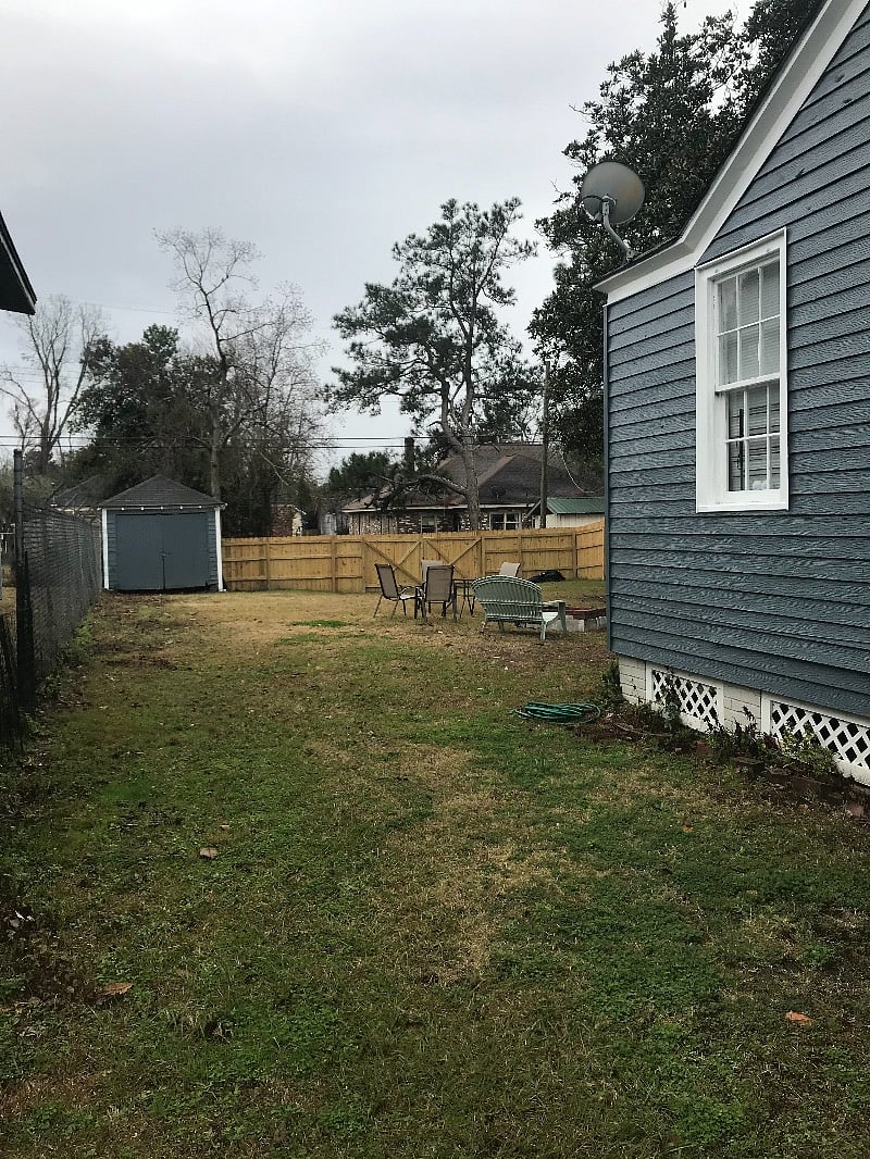 Long fence back yard . A few rustic chairs and a table . 