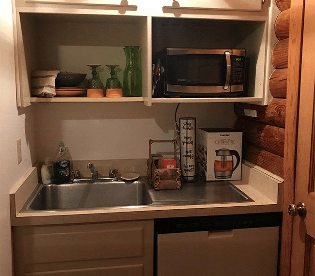 Kitchenette with: microwave, double burner stove, dishwasher, dishes, and electric kettle.