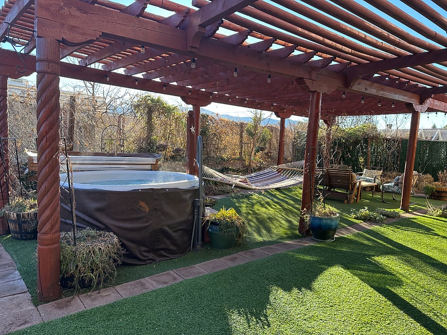 Large shaded outdoor living area with hot tub, hammock, and water feature surrounded by over a dozen trees and vines.