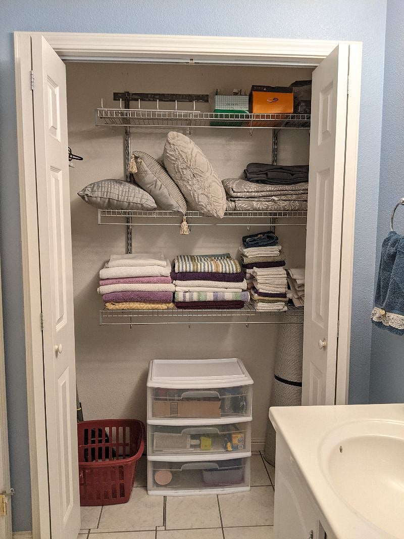 Bathroom closet with linens and towels, ironing board, iron, and kitchenware.