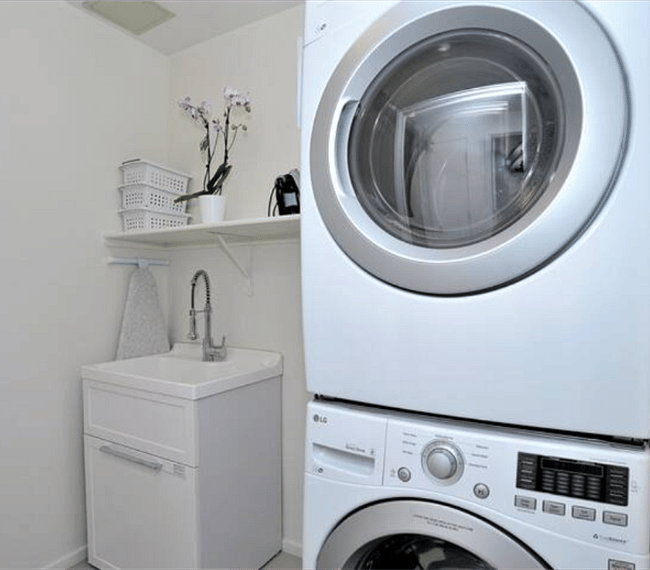 Laundry room with stacked washer+dryer, laundry sink, iron and ironing board.