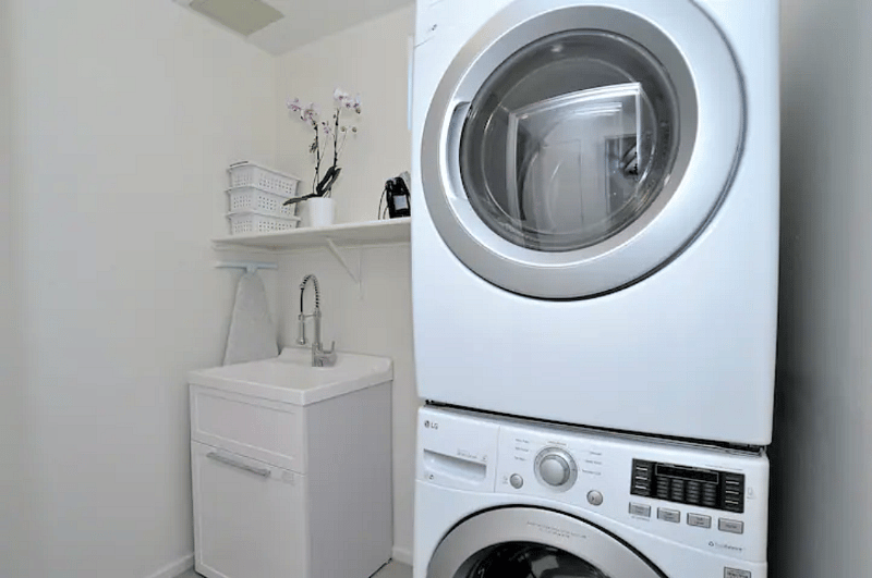 Laundry room with stacked washer+dryer, laundry sink, iron and ironing board.