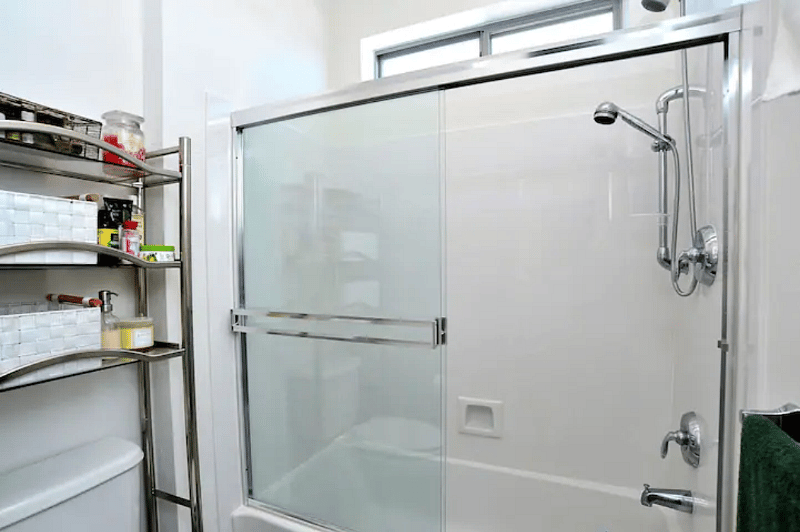 Bathtub with two shower heads and a commode with bidet in a separate section of the bathroom.
