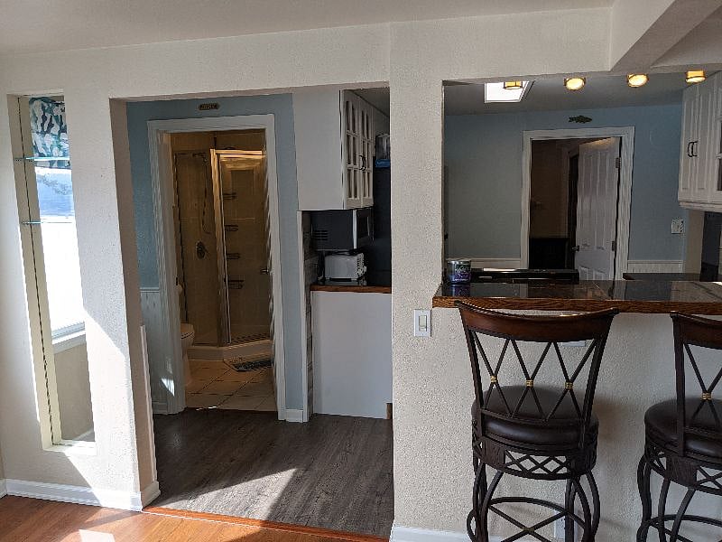 View from dining room over bar seating, kitchen with primary bedroom door on the right and bathroom door on the left