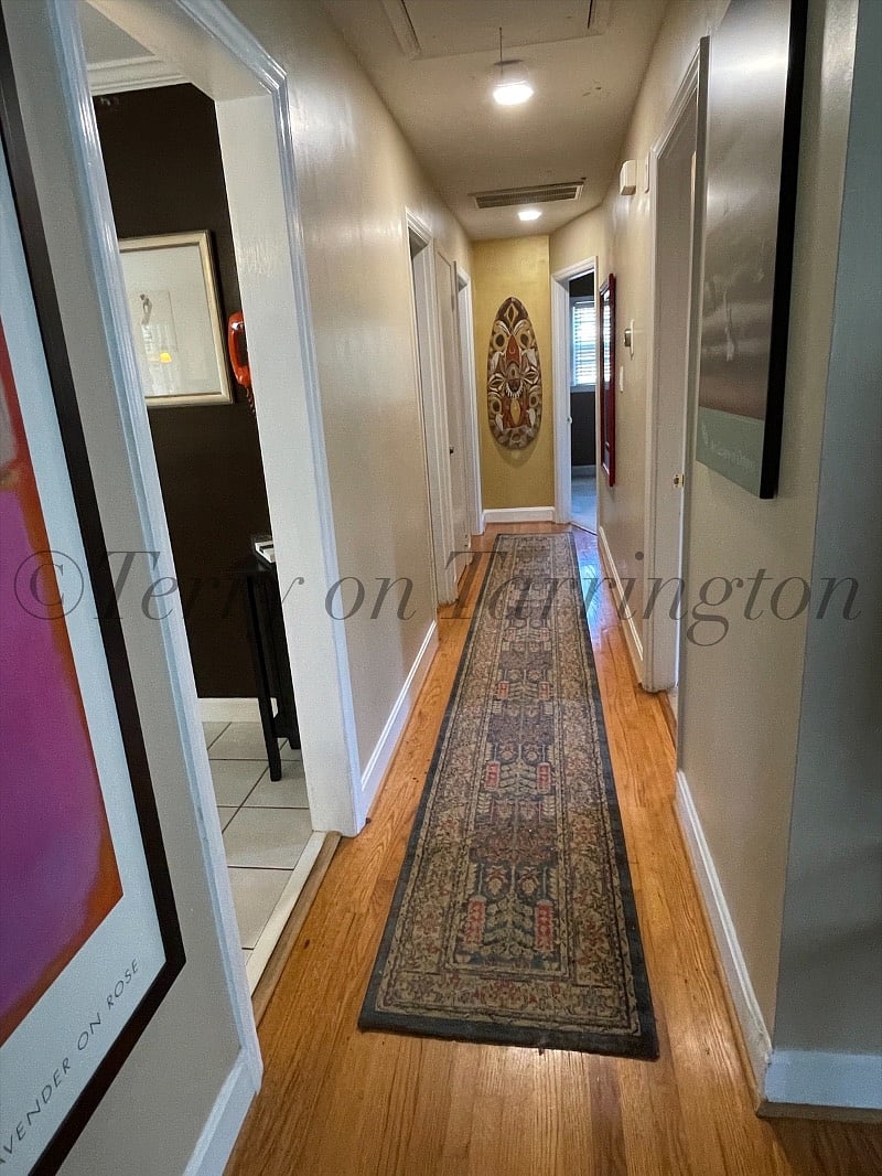 central hallway, from lvng rm, kitchen on left, Bdrm 1 on right (maroon curtains); hall bath (blue) on left in the middle; angled doorway far end on right is the office/guest room (plaid comforter); and master bedrm is far end left (pencil post bed)