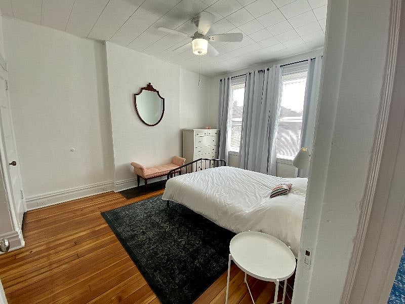 Front bedroom with blackout curtains, ceiling fan, dresser.