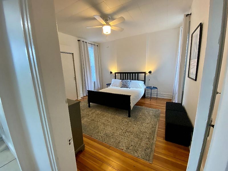 Rear bedroom with blackout curtains, ceiling fan, large closet, and wood floors.