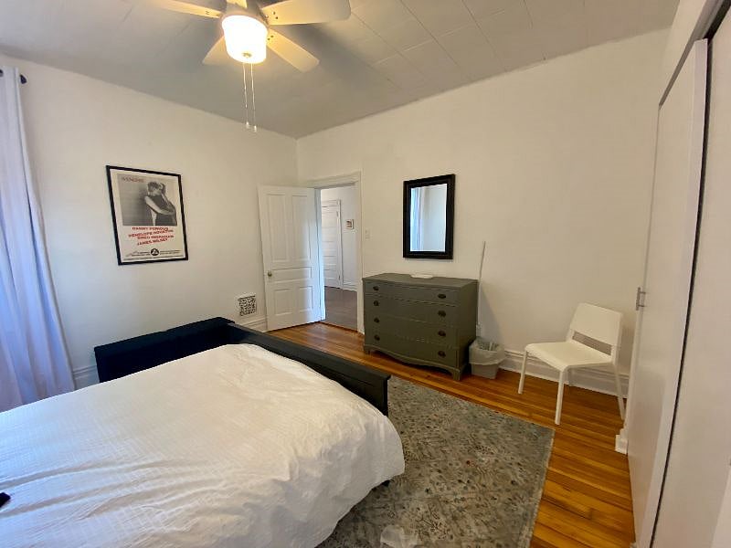 Rear bedroom, with blackout curtains, ceiling fan, large closet, and wood floors.