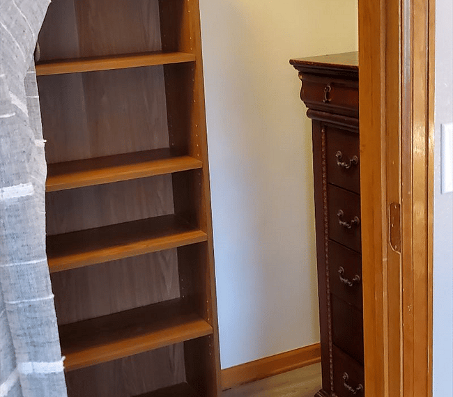 Walk in closet with bookcase, dresser and hanging rod.